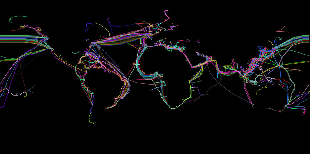 On a black background, lines in random colors indicate the distribution of submarine cables across the globe. Their long shapes make the outlines of continents even more apparent than the dots. There are parallel lines in the upper side of the image and complex knots on the right side.