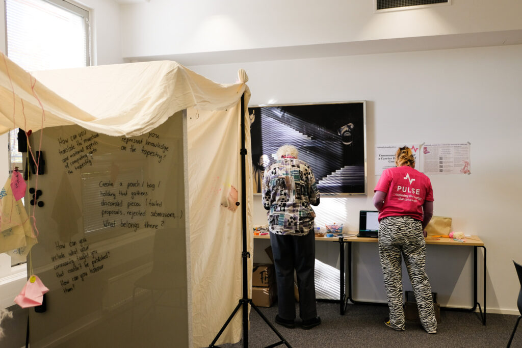 Two conference attendees standing at a table with their back to the camera; next to them is a cloth spanned across tripods and a whiteboard wall.