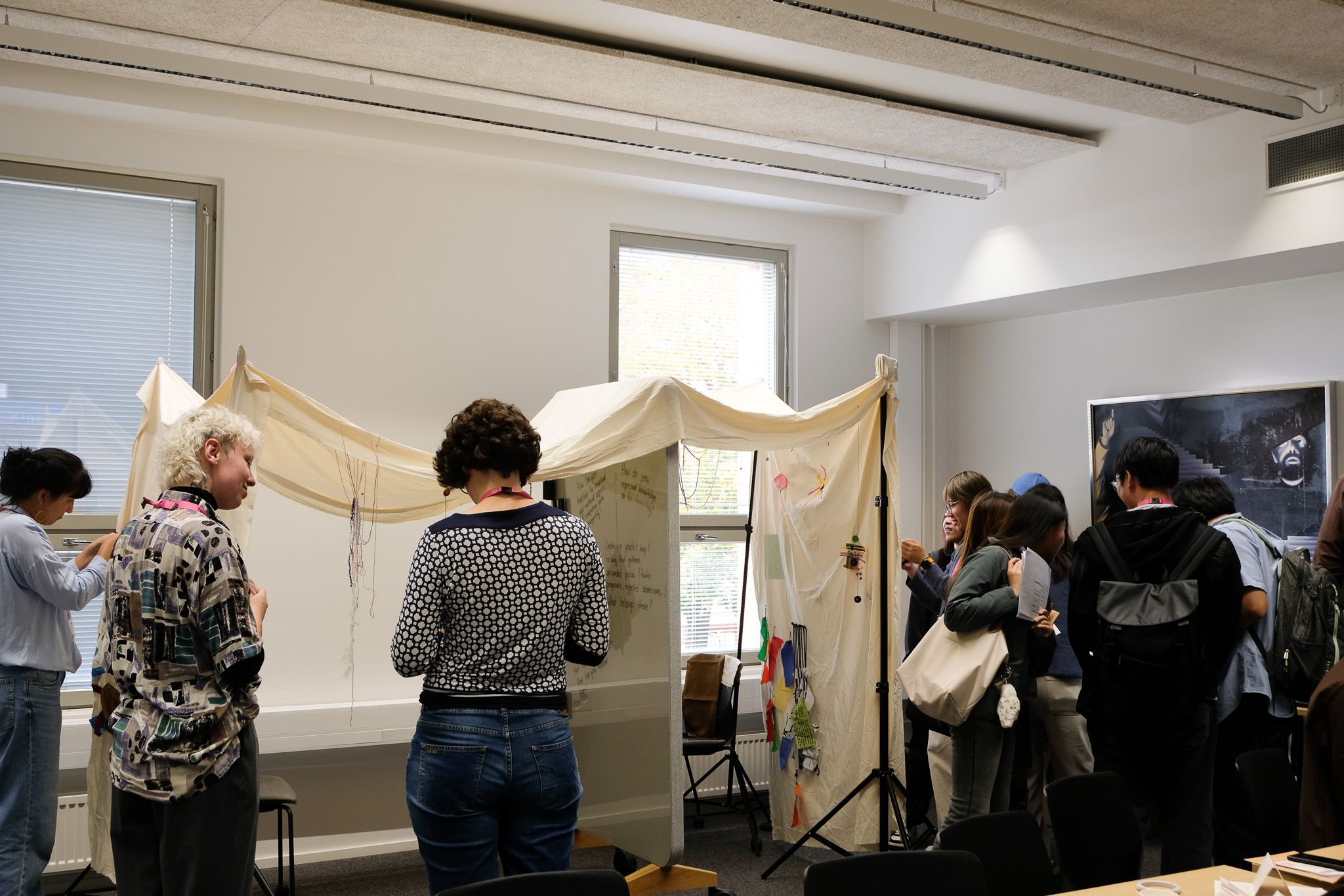 Conference attendees staying in a university classroom, a cloth is spanned across tripods where people are crafting